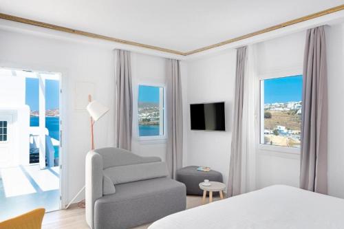 een witte slaapkamer met een stoel en een televisie bij Cape Mykonos in Mykonos-stad