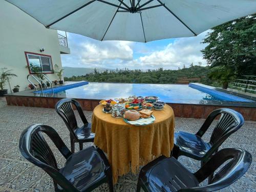 einen Tisch mit einem Teller Essen auf dem Tisch neben einem Pool in der Unterkunft Elsewhere Villa by Hill Staytion in Mahabaleshwar