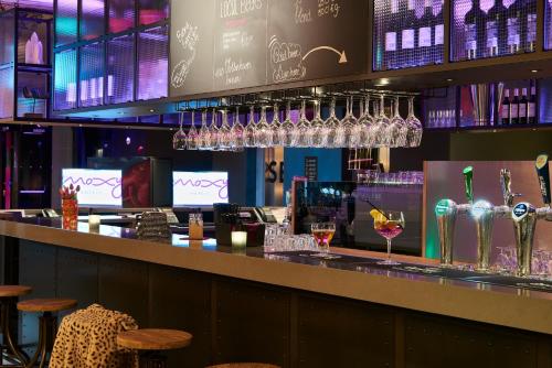 Moxy Amsterdam Schiphol Airport في هوفدوربْ: بار مع كؤوس النبيذ معلقة فوقه