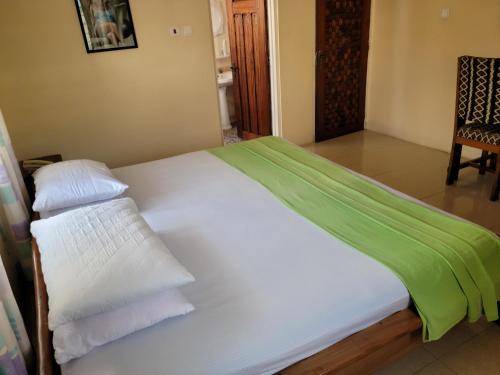 Cama con sábanas verdes y almohadas blancas en Loreto Palm Villa, en Cape Coast