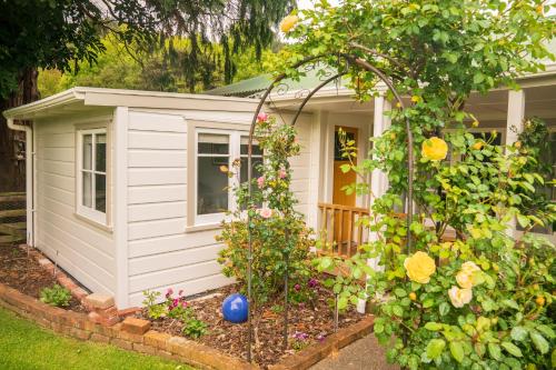 einen kleinen weißen Schuppen mit einem Blumengarten in der Unterkunft Birdsong Cottage in Paraparaumu