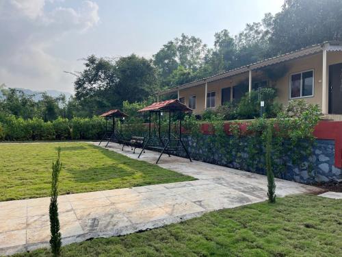 un giardino con due altalene e ombrelloni di fronte a una casa di VRISA Mountain Retreat a Pune