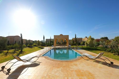 a swimming pool in a park with two chairs at Atlas Widan in Marrakech