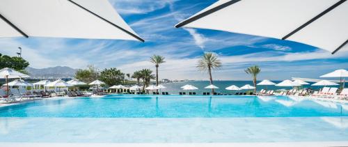 una gran piscina con sombrillas blancas y el océano en Crowne Plaza Muscat, an IHG Hotel, en Mascate