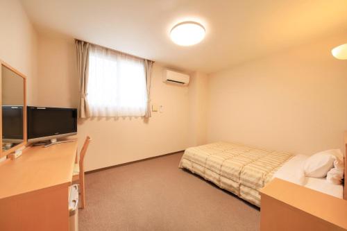 een kamer met een bed en een bureau met een televisie bij Hotel Pony Onsen in Towada