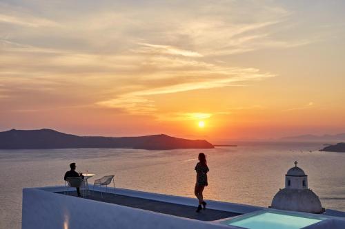 une femme debout au bord d'un toit en regardant le coucher du soleil dans l'établissement Limestone, à Fira