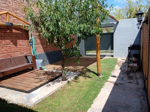 un banco de madera junto a un árbol al lado de un edificio en Alojamiento el Ancla, en San Rafael