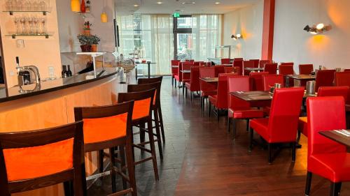 un ristorante con sedie rosse e un bar di Hotel Rhein-Ruhr Bottrop a Bottrop