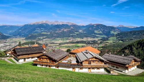 un gruppo di edifici su una collina con montagne sullo sfondo di Chalets Almdorf Haidenberg a Brunico