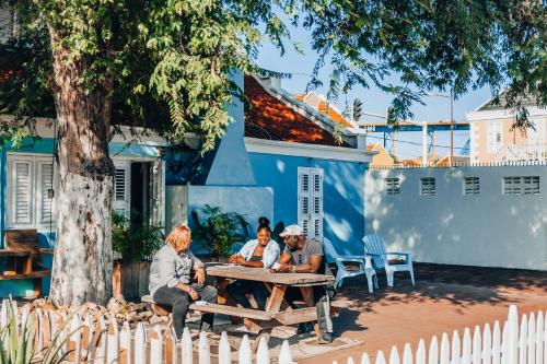 4 personnes assises autour d'une table de pique-nique devant un bâtiment bleu dans l'établissement The Freedom Hotel, à Willemstad