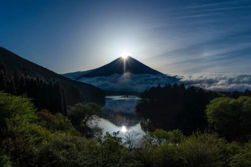 uma montanha com o sol nascendo sobre um lago em Kyukamura Fuji em Fujinomiya