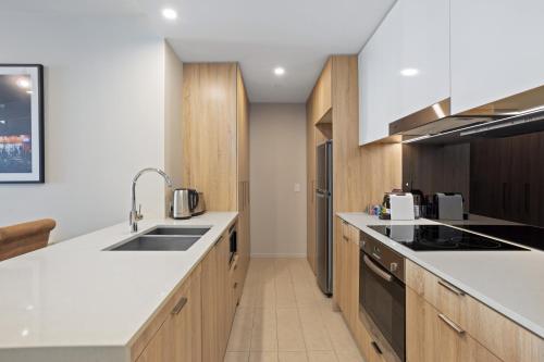 - une cuisine avec des comptoirs blancs et des armoires en bois dans l'établissement Cosy 1-Bed with River Views Pool Gym & BBQ, à Brisbane