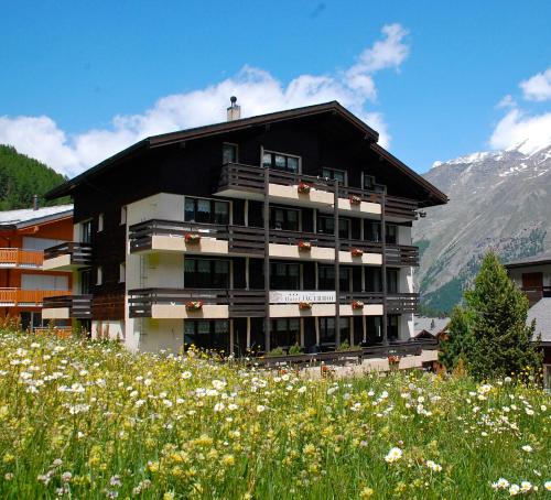 ein Gebäude auf einem Hügel mit einem Blumenfeld in der Unterkunft Hotel Garni Jägerhof in Saas-Fee