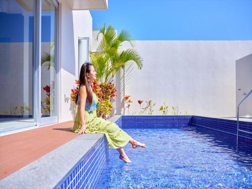 une femme assise au bord d'une piscine dans l'établissement The Pool & Sauna Villa MOTOBU, à Motobu