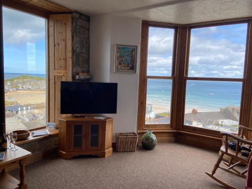 salon z telewizorem z płaskim ekranem i dużymi oknami w obiekcie HUER'S WATCH a beautifully presented PRIVATE APARTMENT with far reaching VIEWS Over ST IVES HARBOUR and BAY and FREE ONSITE PARKING for LARGER GROUPS book along with our Connecting TWO SISTER APARTMENTS w St Ives