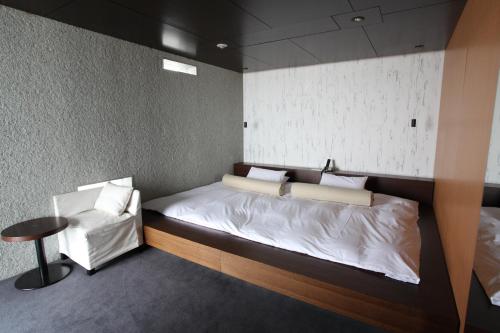 ein kleines Schlafzimmer mit einem Bett und einem Stuhl in der Unterkunft Hotel Setre Kobe Maiko in Kōbe