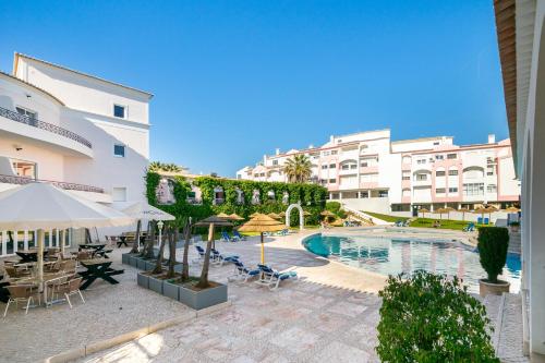 uma piscina com mesas e guarda-sóis ao lado de um edifício em Vilarosa Oceanside by Encantos do Algarve - 1B em Portimão