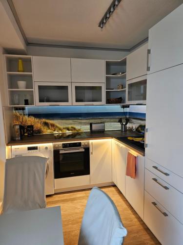 cocina con armarios blancos, mesa y silla en Ferienwohnung im Dachgeschoss mit Aufzug, en Rostock