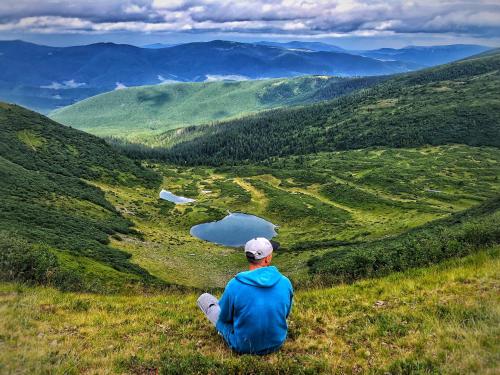 um homem sentado numa colina relvada a olhar para um lago em Pipash em Dragobrat