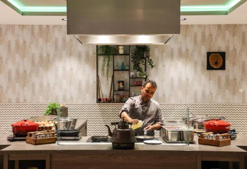 Um homem de pé numa cozinha a preparar comida. em Leonardo Royal Hotel Amsterdam em Amesterdão