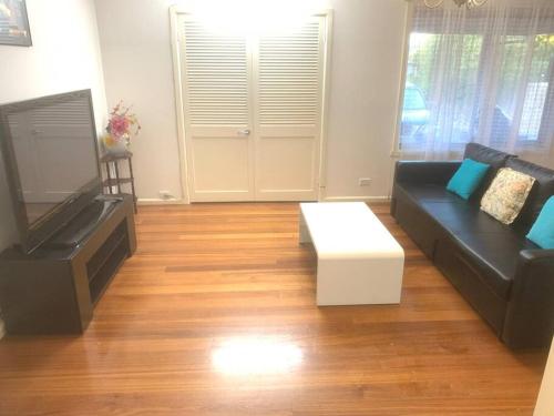 ein Wohnzimmer mit einem schwarzen Sofa und einem TV in der Unterkunft Ideal accommodation in Glen Waverley in Glen Waverley