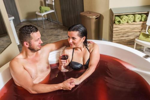 a man and woman in a bath tub with a glass of wine at Malinowy Dwór Hotel Medical SPA in Świeradów-Zdrój