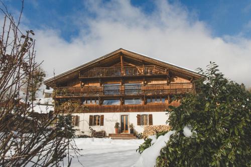 een groot houten huis met een balkon in de sneeuw bij Ferme du Ciel in Samoëns