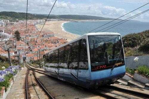 a blue and white train on tracks next to a beach at Rancho Tá-Mar Apartment Nazaré Beach in Nazaré