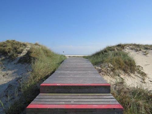 een houten promenade die leidt naar een zandstrand bij Heckenrose-6-Souterrain-links in Norddorf