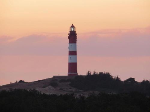 een rode en witte vuurtoren bovenop een heuvel bij Heckenrose-6-Souterrain-links in Norddorf