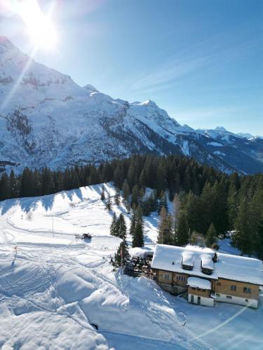 um edifício na neve com montanhas ao fundo em Auberge Restaurant du Lac Retaud em Les Diablerets