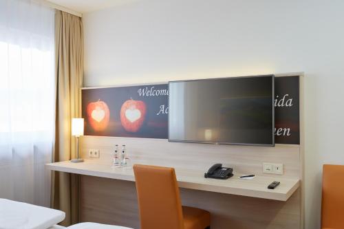 a room with a desk with a television on a wall at H+ Hotel Stuttgart Herrenberg in Herrenberg