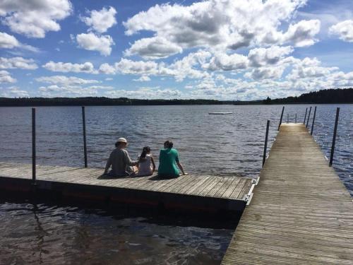 three people sitting on a dock on a lake at Haus Vitsippan in Mariannelund