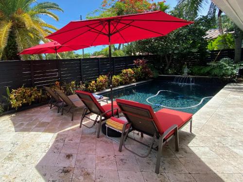 - une table et des chaises avec un parasol rouge à côté de la piscine dans l'établissement Riverbank Guesthouse Wilton Manors, à Fort Lauderdale