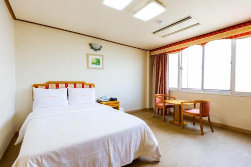 a bedroom with a white bed and a desk and windows at Newvera Hotel in Cheongju