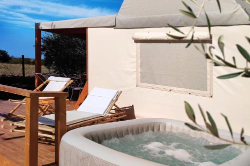 bañera de hidromasaje en una terraza con silla y sombrilla en I Sicomori - Seme di Carota - Glamping e appartamenti con piscina a Saturnia, en Saturnia