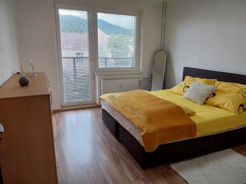 a bedroom with a bed with yellow sheets and two windows at Krásny apartmán v centre Rožňavy in Rožňava