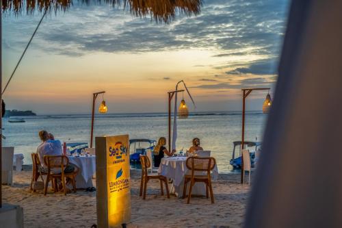 eine Gruppe von Menschen, die am Strand an Tischen sitzen in der Unterkunft Lembongan Beach Club & Resort in Nusa Lembongan