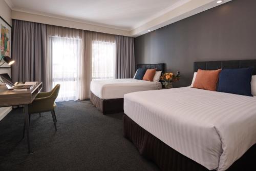 a hotel room with two beds and a desk and a desk at Esplanade Hotel Fremantle - by Rydges in Fremantle