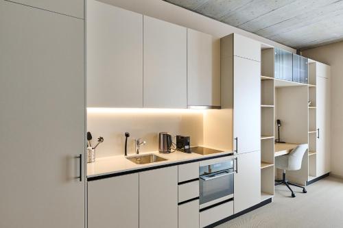 Elle comprend une cuisine avec des placards blancs et un bureau. dans l'établissement Ariv Design Apartments Zug, à Cham