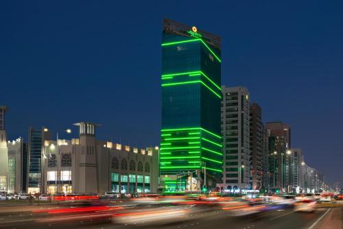 un edificio verde en una ciudad por la noche en La Quinta by Wyndham Abu Dhabi Al Wahda, en Abu Dabi