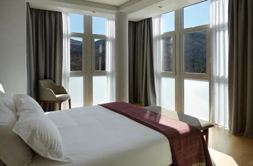 - une chambre avec un lit blanc et de grandes fenêtres dans l'établissement Abrigo da Montanha Hotel Rural, à Sabugueiro