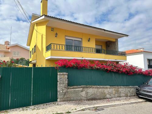 una casa gialla con una recinzione verde e fiori rosa di Bay Golf House a Cascais