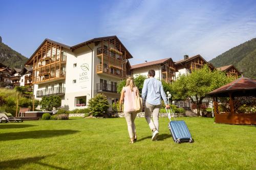 een man en vrouw die in een veld lopen met een koffer bij Hotel Lido - green & slow life in Molveno