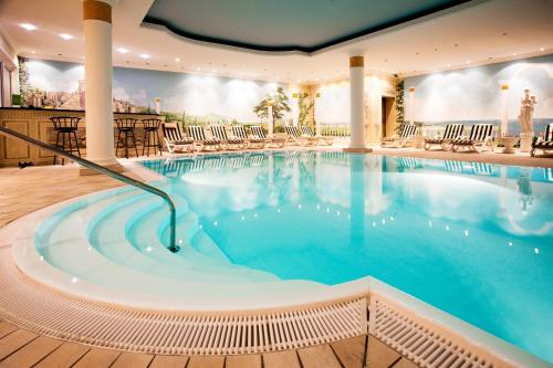 een groot zwembad in een hotel met stoelen bij Atrium Hotel Krüger in Rostock