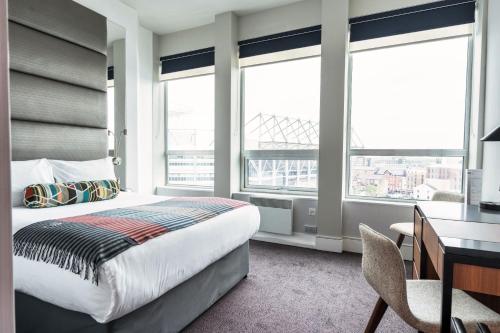 una camera con letto, scrivania e finestre di Sandman Signature Newcastle Hotel a Newcastle upon Tyne