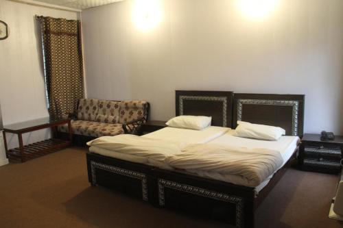 a bedroom with two beds and a chair in it at Malika Kohsar Hotel Murree in Murree