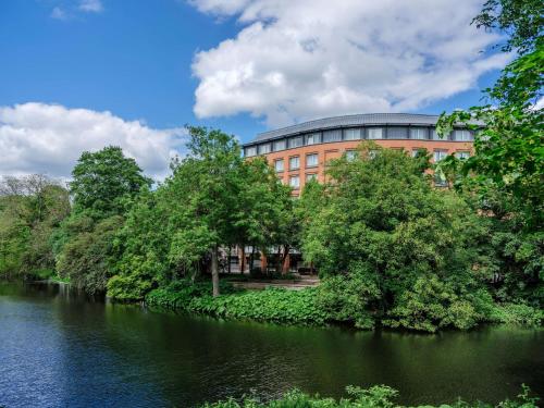 un bâtiment au bord d'une rivière avec des arbres dans l'établissement Dorint Hotel Bremen, à Brême