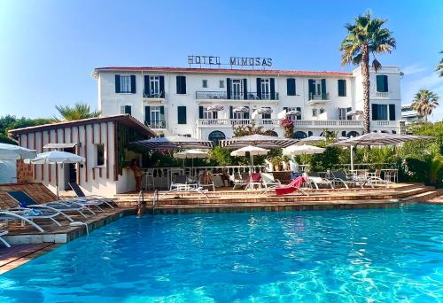 een hotel met een zwembad met stoelen en parasols bij Hotel des Mimosas in Juan-les-Pins