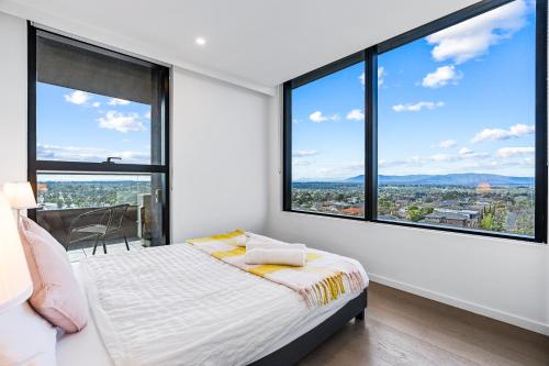 um quarto com janelas grandes e uma cama com lençóis brancos em Skygarden On The Glen em Glen Waverley